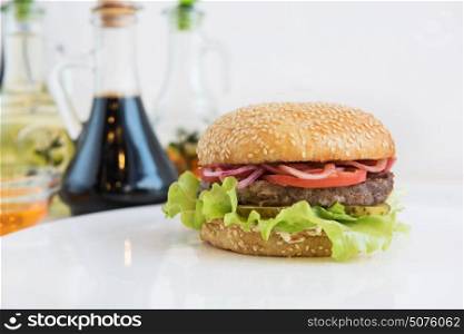 Big tasty burger. Tasty classical burger with meat cheese lettuce onion, tomato and sauce on white table