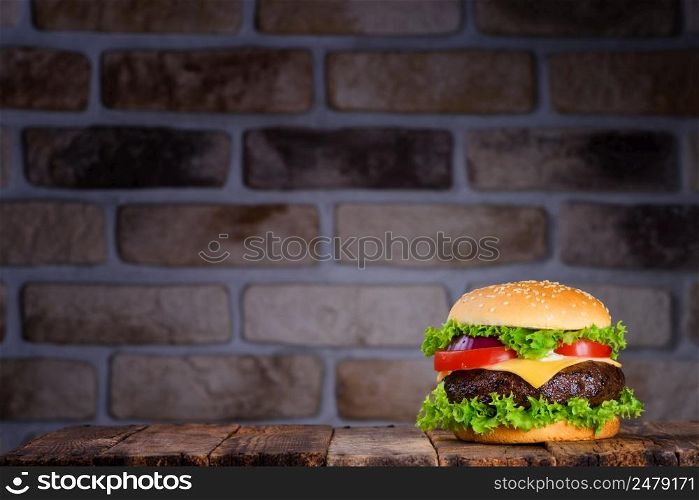 Big tasty classic hamburger on rustic wooden table and brick wall on background horizontal with copy space