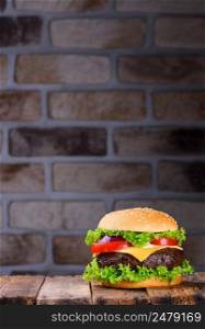 Big tasty classic hamburger on wooden table and brick wall on background with copy space