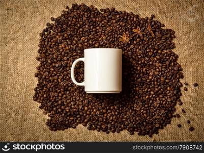 Big white mug lying on pile of roasted coffee beans on linen cloth