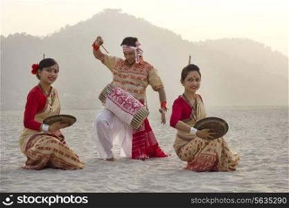 Bihu women dancing with brass plates as Bihu man plays on a dhol