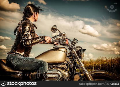 Biker girl in a leather jacket on a motorcycle looking at the sunset.