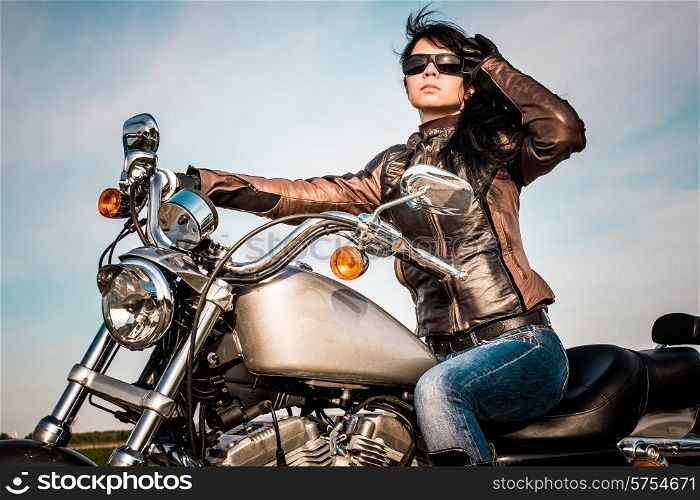 Biker girl in a leather jacket on a motorcycle looking at the sunset.