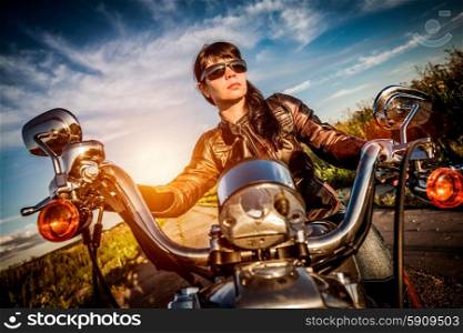 Biker girl in a leather jacket on a motorcycle looking at the sunset. Filter applied in post-production.