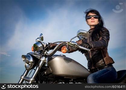 Biker girl in a leather jacket on a motorcycle looking at the sunset.