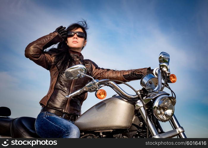 Biker girl in a leather jacket on a motorcycle looking at the sunset.