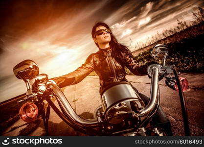 Biker girl in a leather jacket on a motorcycle looking at the sunset. Filter applied in post-production.