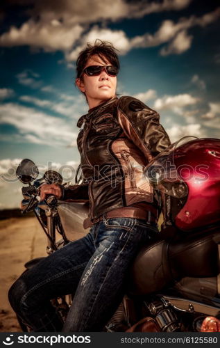 Biker girl in a leather jacket on a motorcycle looking at the sunset.