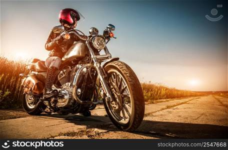 Biker girl on a motorcycle in a leather jacket and a helmet, looks at the way