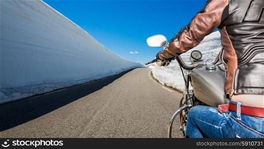 Biker girl rides a mountain road with high snow wall in Norway. First-person view.