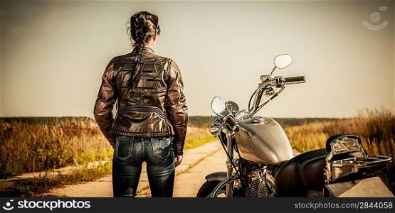 Biker girl stands on the road and looks into the distance