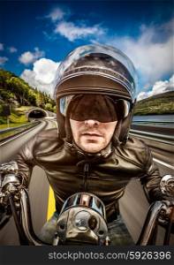 Biker in helmet and leather jacket racing on the road.