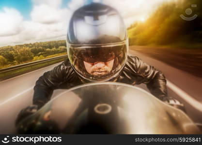 Biker in helmet and leather jacket racing on the road. Filter applied in post-production.