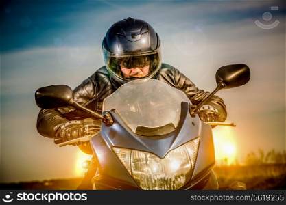 Biker in helmet and leather jacket racing on the road with the sun in the background