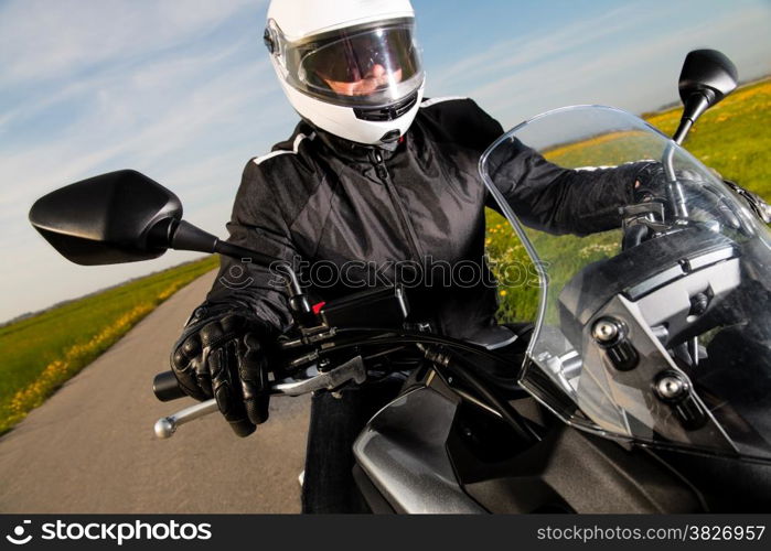 Biker in helmet and leather jacket riding on the road.