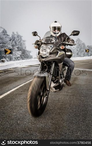 Biker in helmet and leather jacket riding on the road with snow.