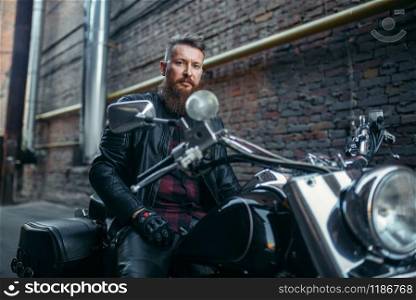 Biker in leather jacket sitting on classical chopper. Vintage bike, rider on motorcycle, two-wheeled transport. Biker in leather jacket on classical chopper