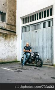 Biker looking mobile sitting on a custom motorcycle in front of the garage door. Biker looking mobile sitting on motorcycle