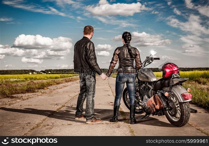 Biker man and girl stands on the road and looks into the distance