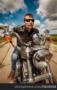 Biker man wearing a leather jacket and sunglasses sitting on his motorcycle and racing on the road.