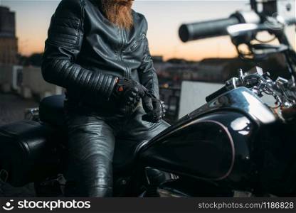 Biker poses on a motorcycle in city on sunset, classical chopper. Vintage bike, freedom lifestyle, biking