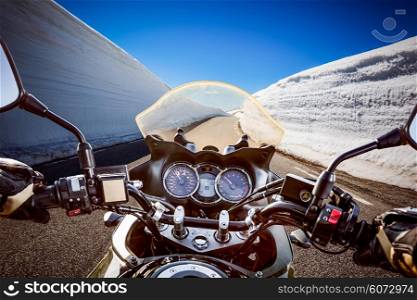 Biker rides a mountain road with high snow wall in Norway. First-person view.