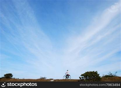 Biking man in a plain landscape with blue sky and a lot of space