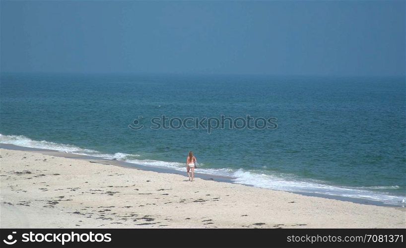 Bikini clad woman walking along Ho Hum beach on Fire Island