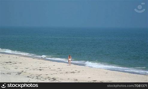 Bikini clad woman walking along Ho Hum beach on Fire Island