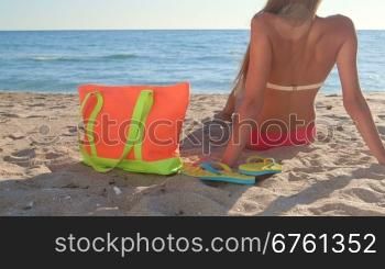 Bikini girl with colorful accessories on sandy beach rear view