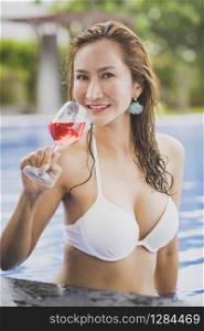 bikini woman and glass of red beverage in swimming pool