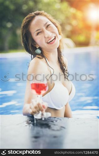 bikini woman and glass of red beverage in swimming pool