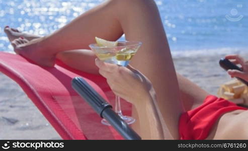 Bikini woman with cocktail glass relaxing on tropical beach close-up