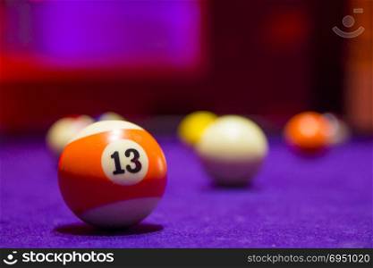 Billiard balls in a pool table. focus on the orange number 13 ball.