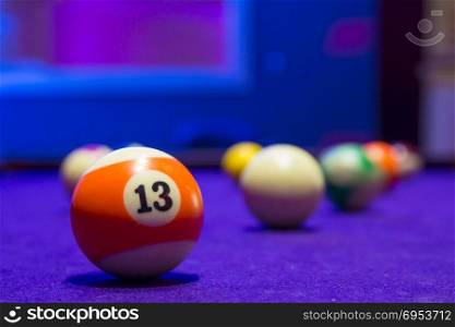 Billiard balls in a pool table. focus on the orange number 13 ball.