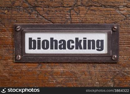 biohacking - managing one&rsquo;s own biology using a combination of medical, nutritional and electronic techniques - file cabinet label, bronze holder against grunge and scratched wood