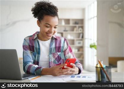 Biracial teen girl chatting online on smartphone while doing homework. Schoolgirl holding phone, distracted from studying learning. New generations addicted with social networks, overuse of gadgets.. Biracial teen girl hold phone distracted from studying. Social network addiction, overuse of gadgets