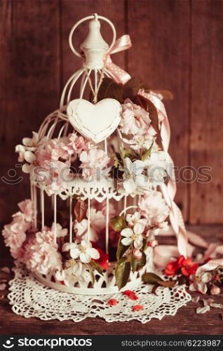 Bird cage with wooden heart with sakura and apple flowers. Wedding decorations with pink ribbon with copy space. Bird cage with wooden heart