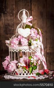 Bird cage with wooden heart with sakura and apple flowers. Wedding decorations with pink ribbon