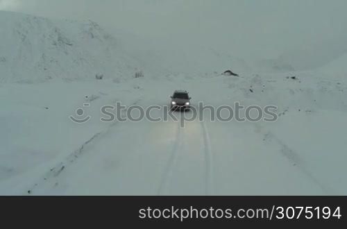 Bird eye view of silver car driving on the snow-covered road through the mountains
