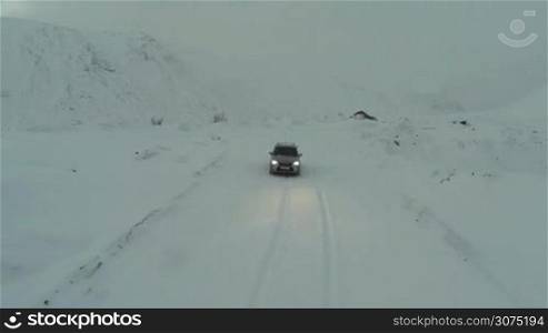 Bird eye view of silver car driving on the snow-covered road through the mountains