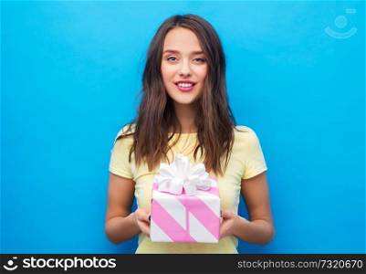 birthday and people concept - smiling young woman or teenage girl in yellow t-shirt with gift box over bright blue background. young woman or teenage girl with birthday gift
