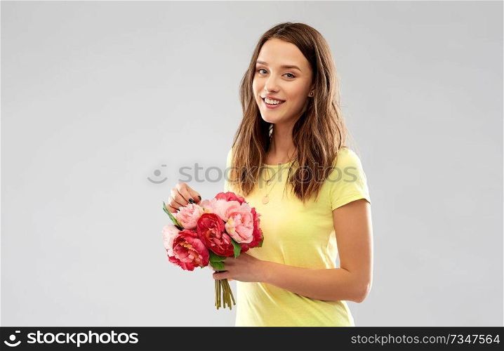 birthday and people concept - smiling young woman or teenage girl in yellow t-shirt with flower bouquet over grey background. young woman or teenage girl with flower bouquet