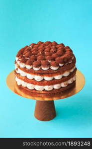 Birthday cake on the wooden cake stand. Beautiful chocolate sponge cake with whipped cream garnished with sprinkled cocoa. Blue background. Copy space. Food photography for recipe.