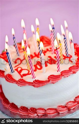 Birthday cake with burning candles and icing on pink background