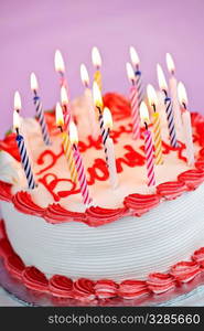 Birthday cake with burning candles and icing on pink background