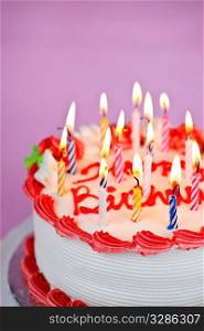 Birthday cake with burning candles and icing on pink background