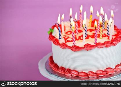 Birthday cake with burning candles on a plate on pink background
