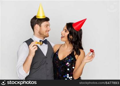 birthday, celebration and holidays concept - happy couple with party blowers and caps having fun. happy couple with party blowers having fun. happy couple with party blowers having fun