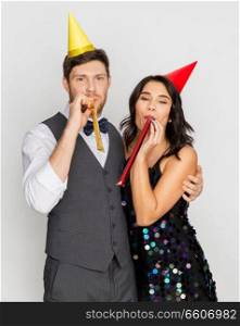 birthday, celebration and holidays concept - happy couple with party blowers and caps having fun. happy couple with party blowers having fun